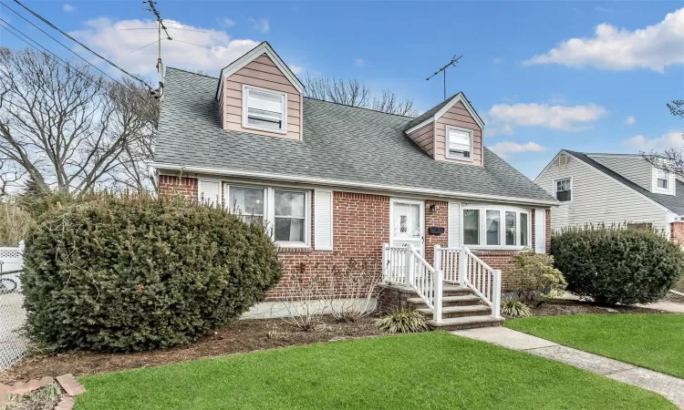 Cape cod house with brick siding, roof with shingles, and a front yard