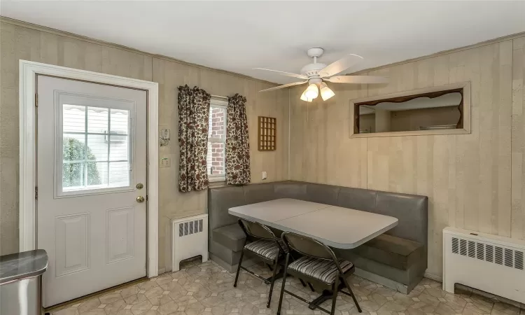 Dining room featuring breakfast area, wooden walls, radiator heating unit, and a ceiling fan