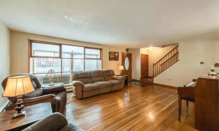 Living area featuring baseboards, a baseboard heating unit, wood finished floors, and an AC wall unit