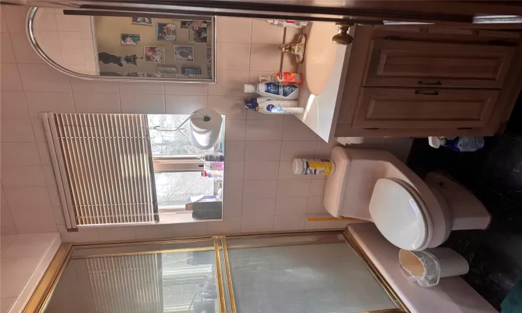 Bathroom with vanity, toilet, tile walls, and bath / shower combo with glass door