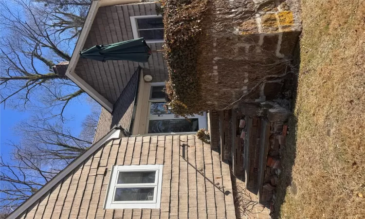 Property entrance featuring a lawn, roof with shingles, and a chimney