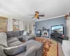 Carpeted living room with a stone fireplace, baseboards, crown molding, and a ceiling fan