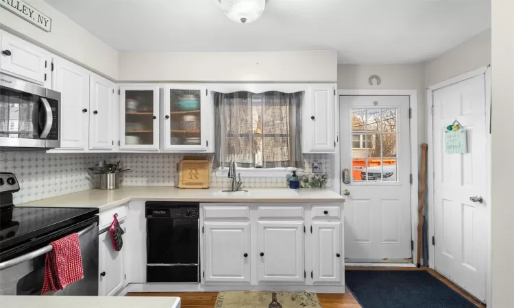 Kitchen with decorative backsplash, light countertops, white cabinets, and stainless steel appliances