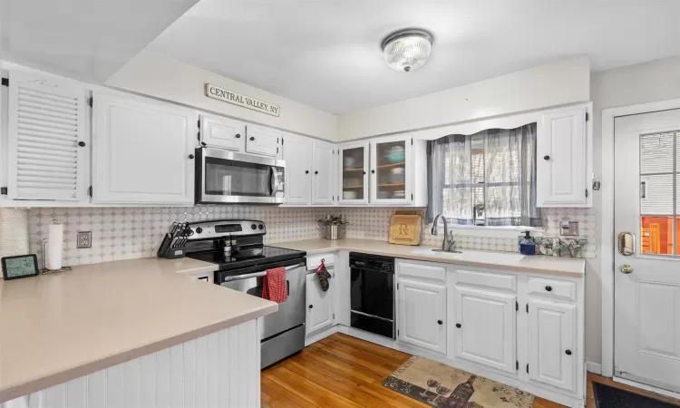 Kitchen with light wood finished floors, appliances with stainless steel finishes, white cabinetry, and light countertops