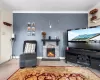 Carpeted living area featuring a stone fireplace, crown molding, and baseboards