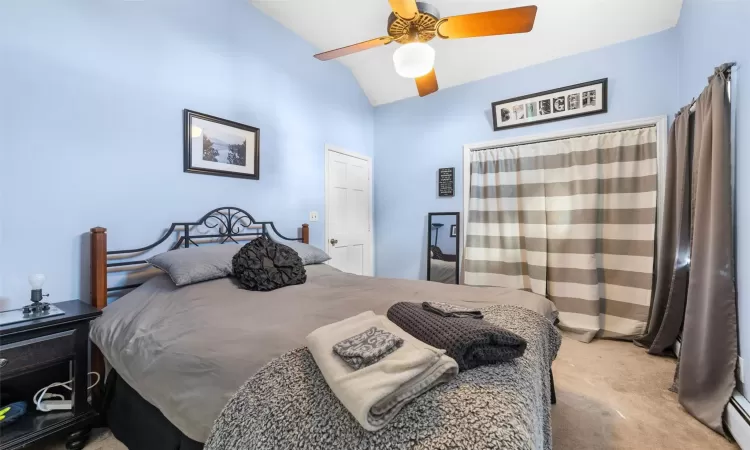 Carpeted bedroom featuring baseboard heating, ceiling fan, and vaulted ceiling