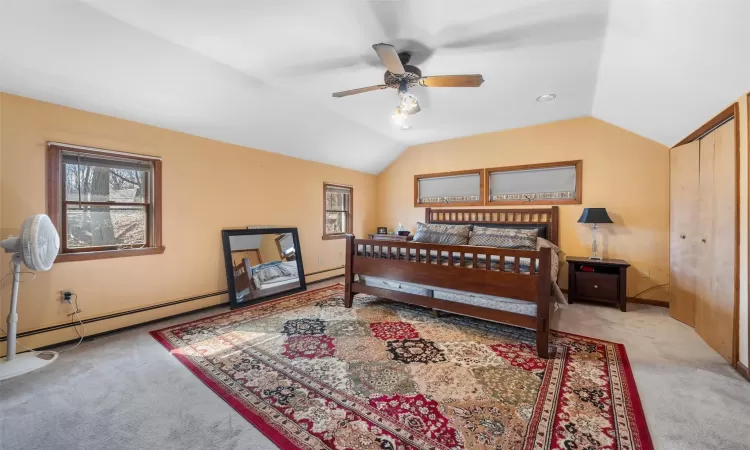 Bedroom with a baseboard heating unit, lofted ceiling, and carpet floors