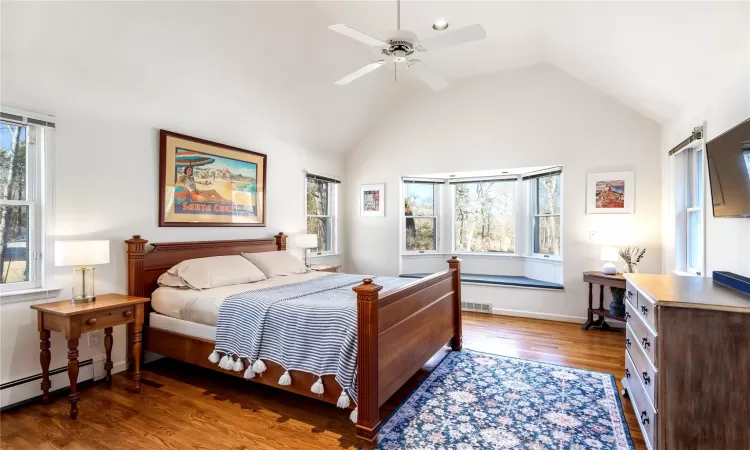 Bedroom with multiple windows, wood finished floors, visible vents, and baseboard heating