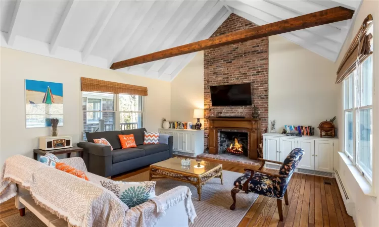 Living area featuring beam ceiling, baseboard heating, a fireplace, and hardwood / wood-style floors