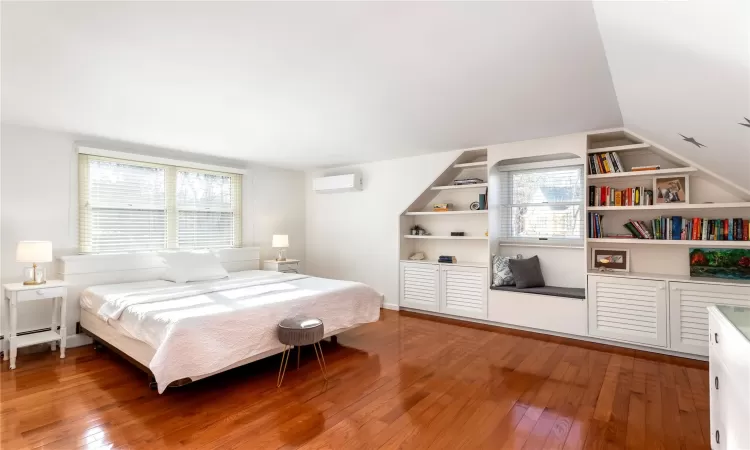 Bedroom with vaulted ceiling, light wood-style flooring, and a wall mounted AC