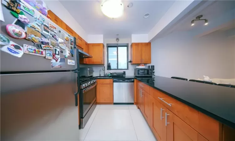 Kitchen featuring ventilation hood, light tile patterned floors, appliances with stainless steel finishes, brown cabinetry, and a sink