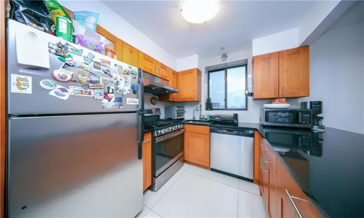 Kitchen with brown cabinets, under cabinet range hood, a sink, appliances with stainless steel finishes, and light tile patterned floors