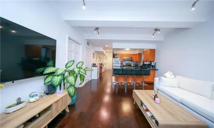 Living area featuring dark wood-style floors, beam ceiling, and track lighting