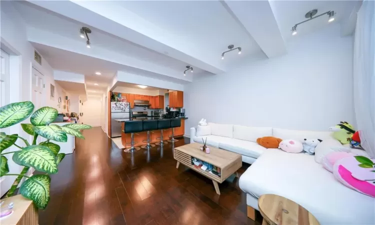 Living room featuring beamed ceiling, visible vents, track lighting, and hardwood / wood-style flooring