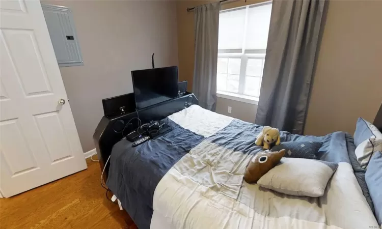 Bedroom with electric panel, baseboards, and wood finished floors