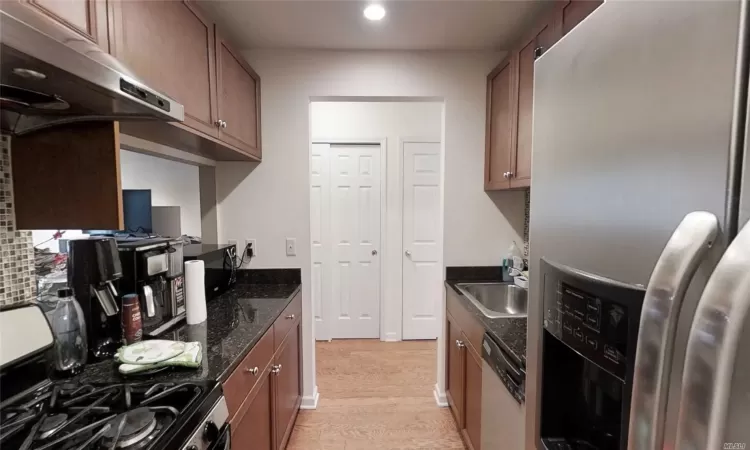 Kitchen featuring dishwashing machine, gas stove, a sink, under cabinet range hood, and stainless steel fridge