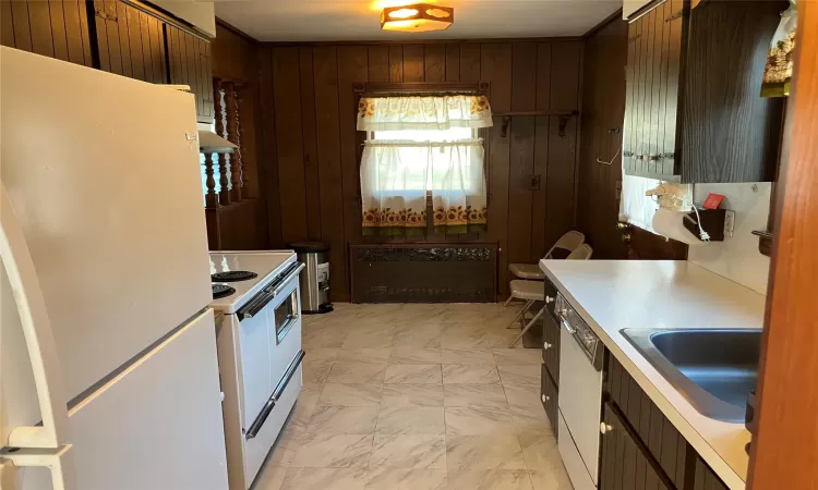 Kitchen featuring under cabinet range hood, a sink, white appliances, wood walls, and light countertops