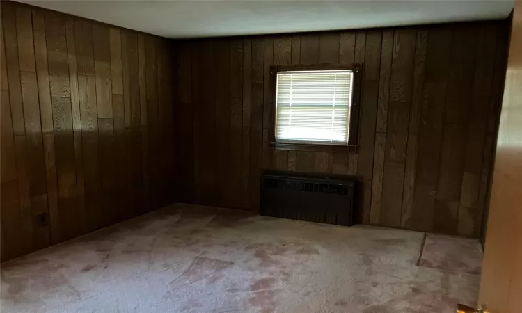 Carpeted empty room with wooden walls and radiator heating unit