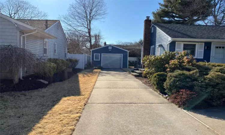 View of side of home featuring a detached garage, fence, a chimney, an outdoor structure, and driveway