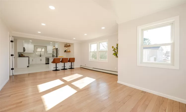 Living area with crown molding, light wood-style floors, baseboards, and baseboard heating