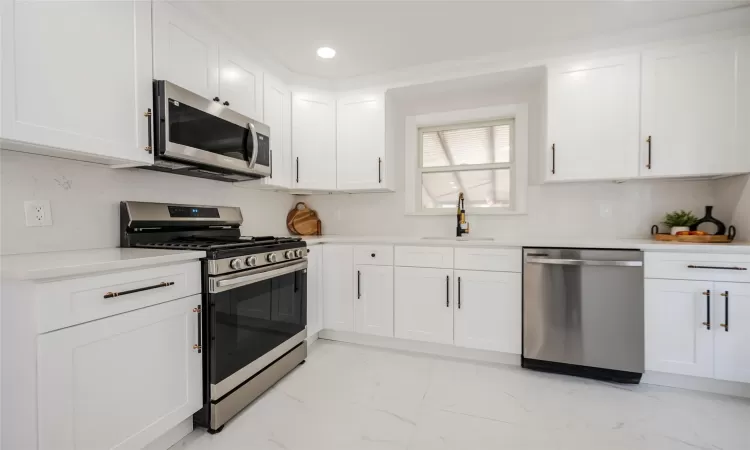 Kitchen with marble finish floor, a sink, white cabinetry, stainless steel appliances, and light countertops