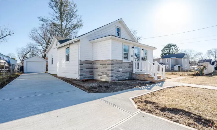 View of front of property featuring a garage, stone siding, an outdoor structure, and concrete driveway