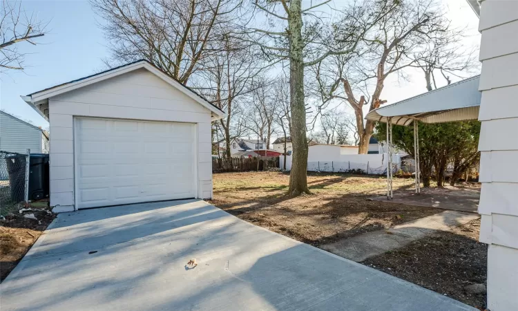 View of yard featuring a garage, an outdoor structure, driveway, and fence