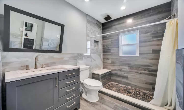 Full bath featuring a tile shower, toilet, vanity, and tile walls