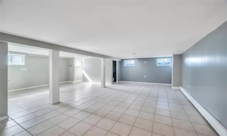 Below grade area featuring light tile patterned floors, a healthy amount of sunlight, baseboards, and baseboard heating