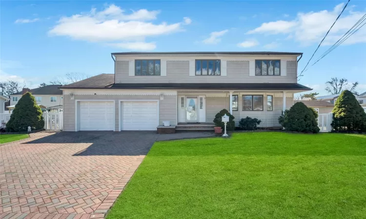 Traditional-style home with a front yard, decorative driveway, fence, and a garage