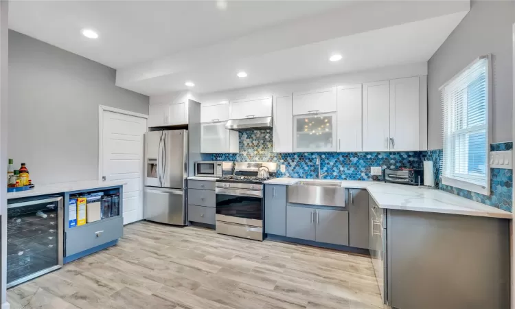 Kitchen featuring under cabinet range hood, light stone counters, a sink, wine cooler, and appliances with stainless steel finishes