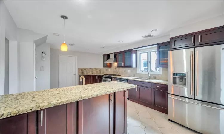 Kitchen featuring a sink, decorative backsplash, glass insert cabinets, appliances with stainless steel finishes, and wall chimney range hood