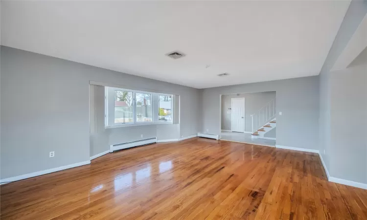 Spare room featuring stairway, wood finished floors, visible vents, and baseboard heating