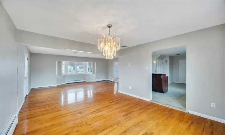 Unfurnished room featuring light wood-style floors, baseboard heating, and a notable chandelier