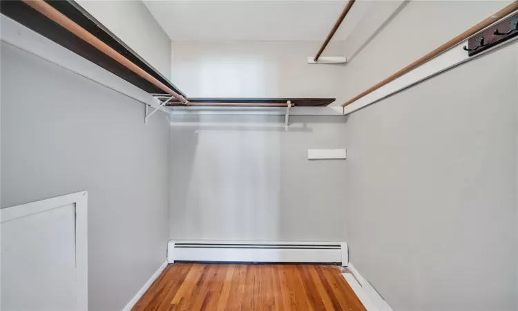 Walk in closet with wood finished floors and a baseboard radiator