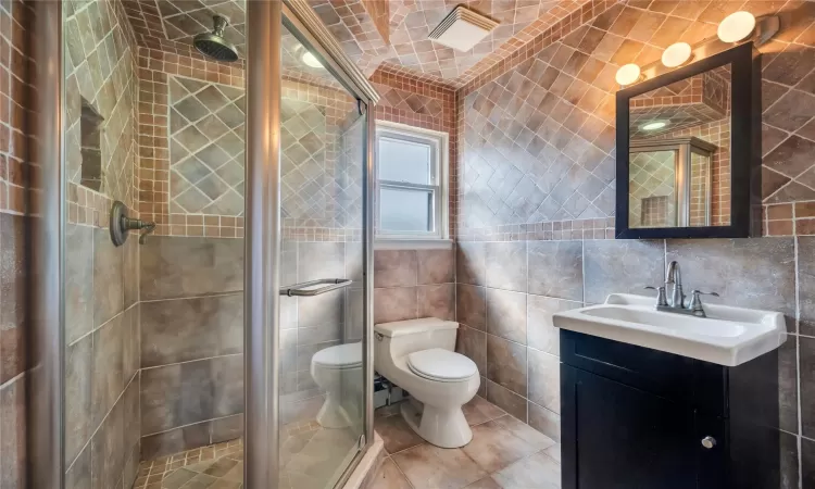 Full bathroom featuring tile patterned flooring, a shower stall, tile walls, toilet, and vanity