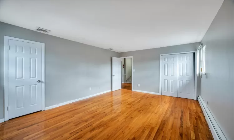 Unfurnished bedroom featuring wood finished floors, visible vents, baseboards, a closet, and a baseboard heating unit