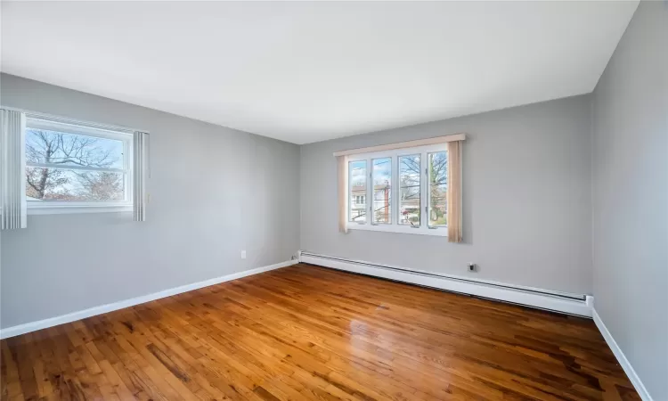 Unfurnished room with a baseboard heating unit, baseboards, and hardwood / wood-style floors