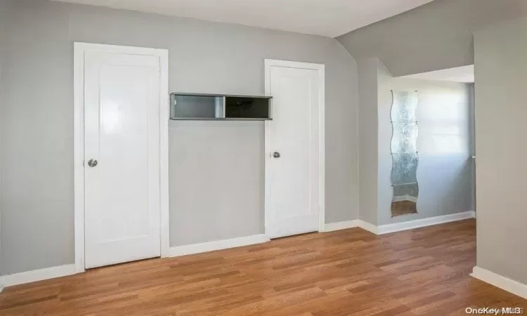 Unfurnished bedroom with vaulted ceiling, baseboards, and wood finished floors