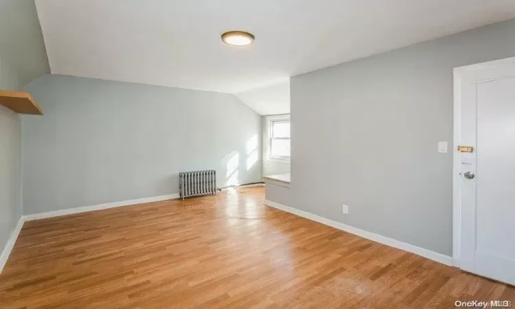 Spare room with vaulted ceiling, radiator, light wood-style floors, and baseboards