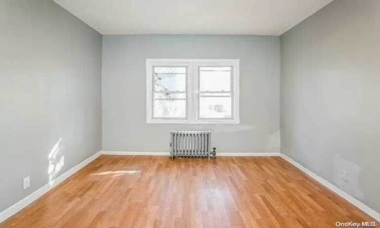 Unfurnished room featuring light wood finished floors, radiator, and baseboards