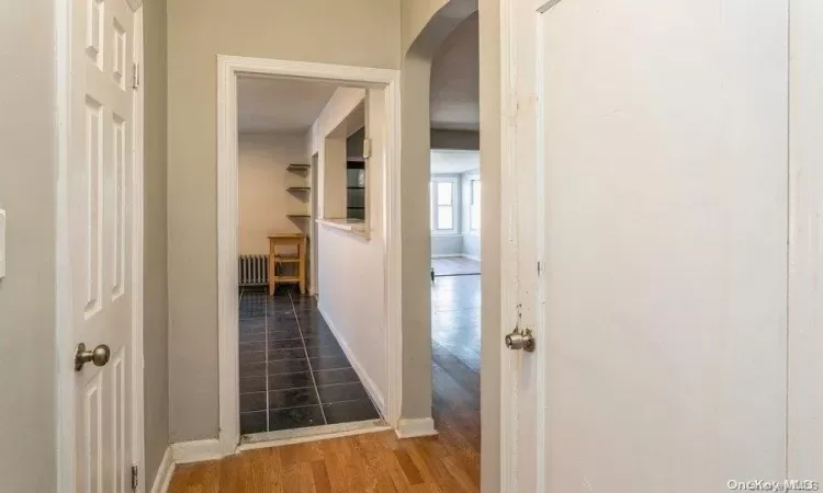 Hallway featuring radiator heating unit, wood finished floors, arched walkways, and baseboards