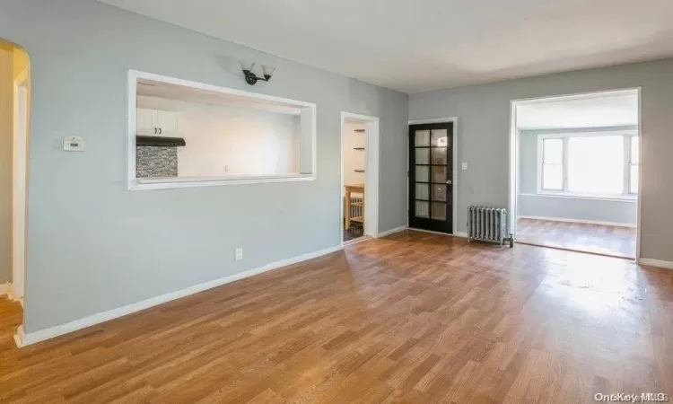 Spare room featuring baseboards, radiator, arched walkways, and light wood finished floors