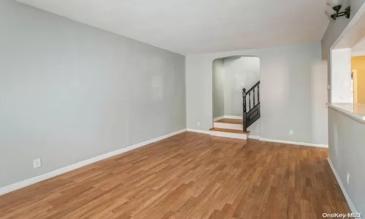 Empty room with stairway, baseboards, arched walkways, and light wood finished floors