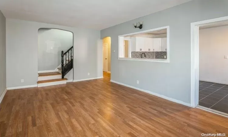 Unfurnished living room featuring stairway, wood finished floors, arched walkways, and baseboards