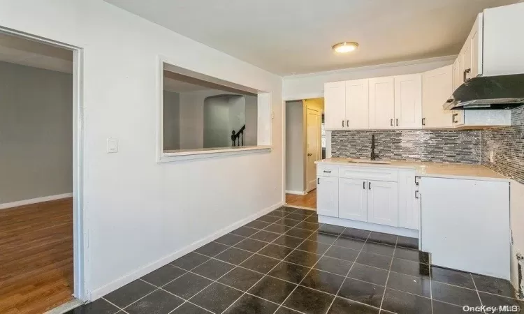 Kitchen featuring dark tile patterned flooring, a sink, white cabinets, light countertops, and decorative backsplash