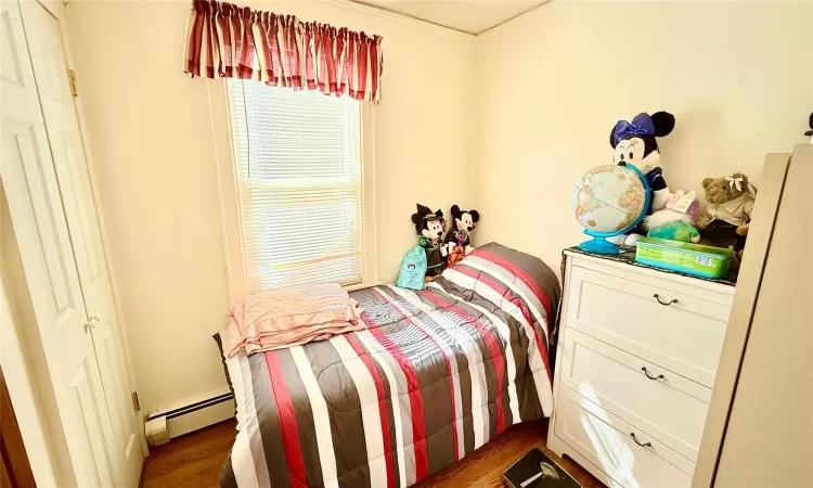 Bedroom featuring a baseboard heating unit and dark wood-style flooring