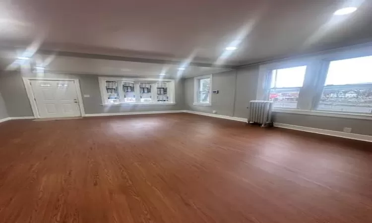 Empty room featuring a healthy amount of sunlight, radiator, and dark colored carpet