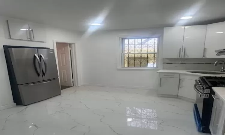 Kitchen with freestanding refrigerator, a sink, black gas range, white cabinetry, and marble finish floor