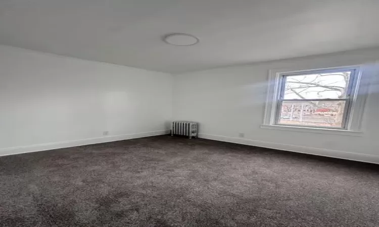 Empty room featuring radiator, baseboards, and dark colored carpet